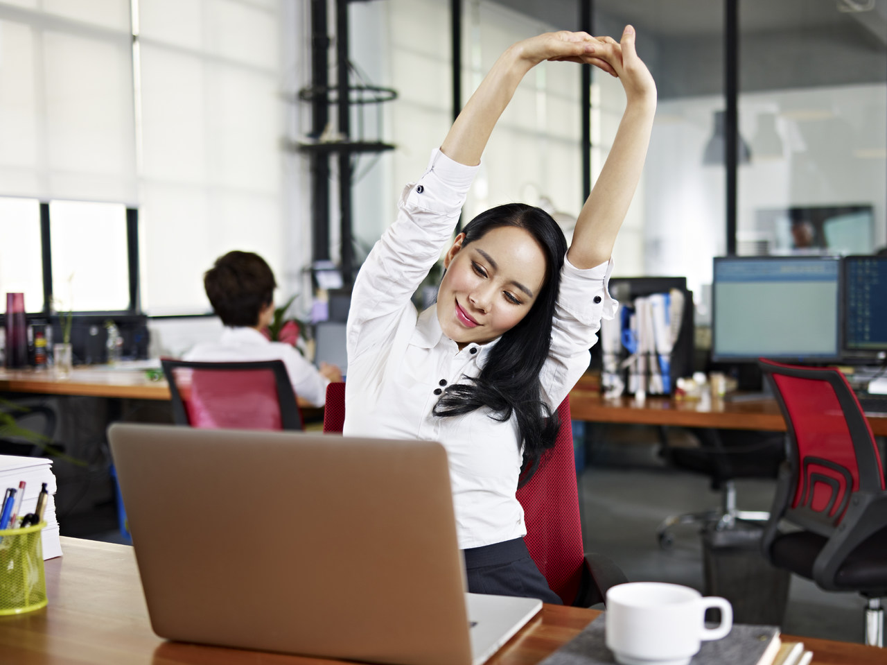 Ofis ortamında bilgisayar karşısında kollarını esneten kadın