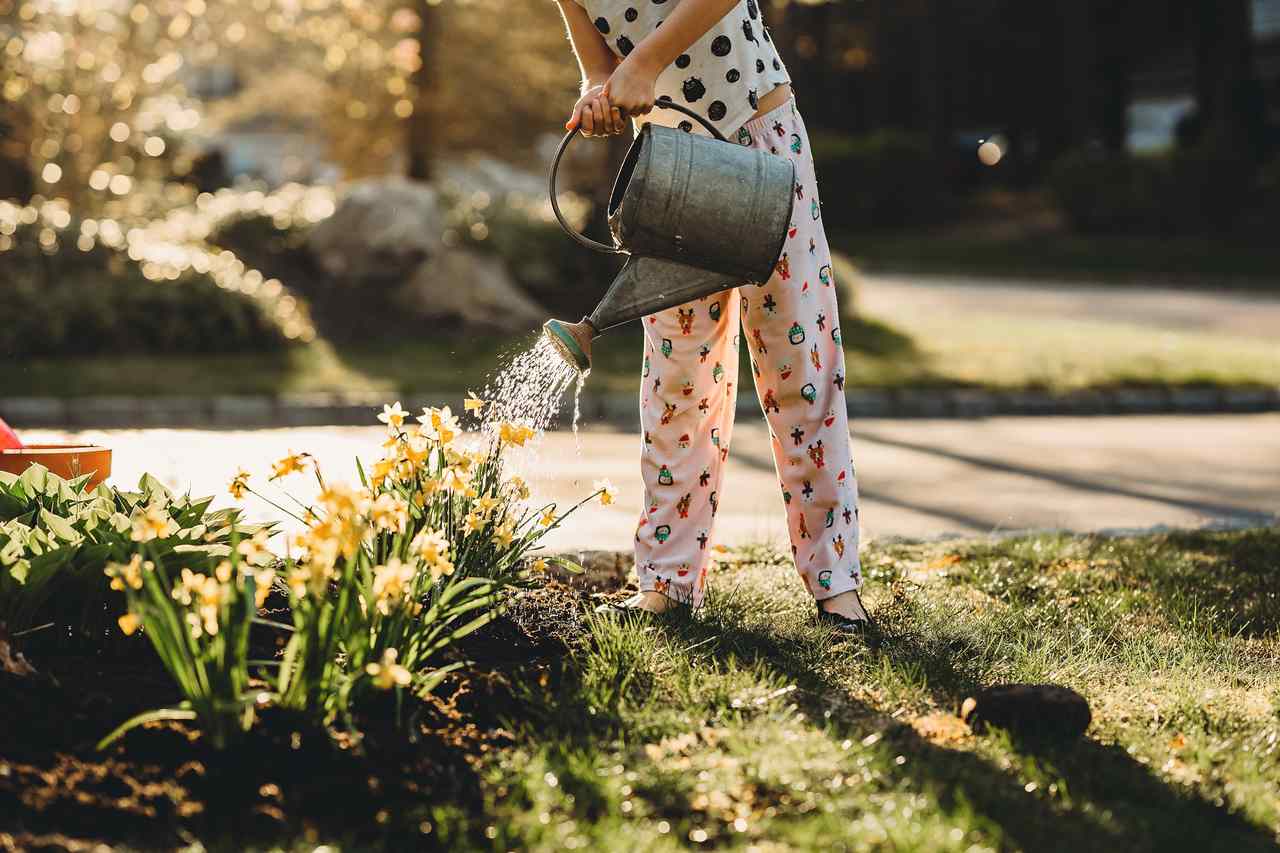 bahçedeki çiçekleri sulayan puantiye desenli pijamalı kadın